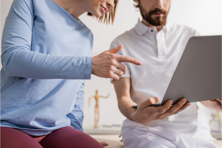 partial view of woman pointing at laptop near physical therapist