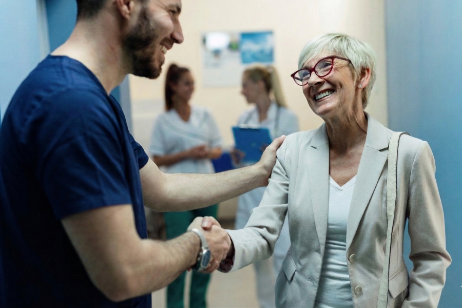Clinician warmly greeting a patient in a clinic hallway, illustrating improved patient engagement and satisfaction supported by efficient clinical documentation with ScribePT AI scribing.