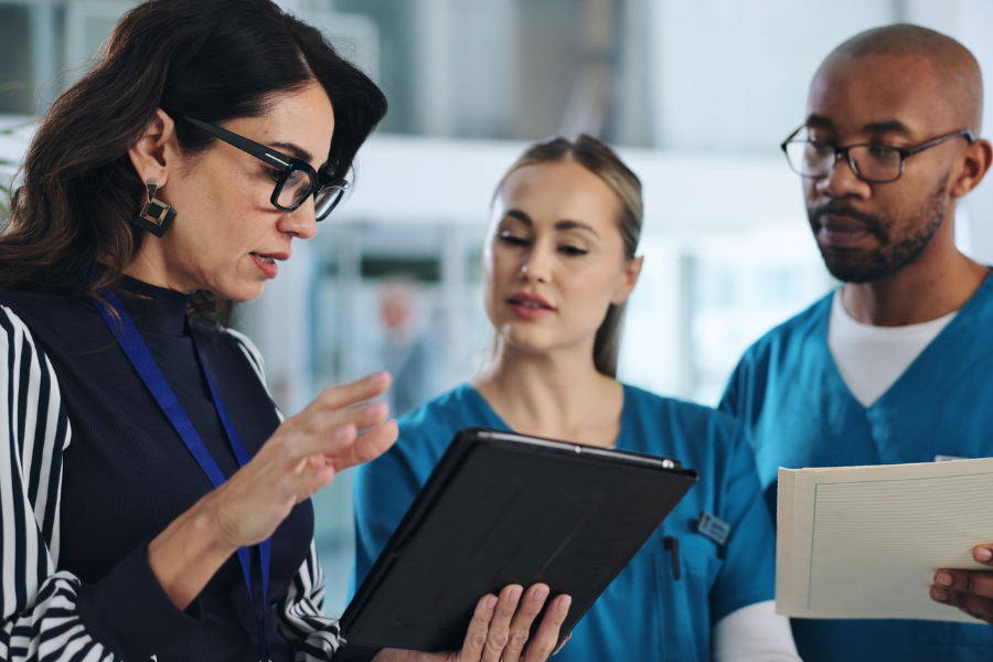 Healthcare professionals discussing patient care using a tablet in a clinic, showcasing collaboration and modern technology in healthcare workflows. AI solutions like ScribePT enhance clinical decision-making and streamline documentation processes.