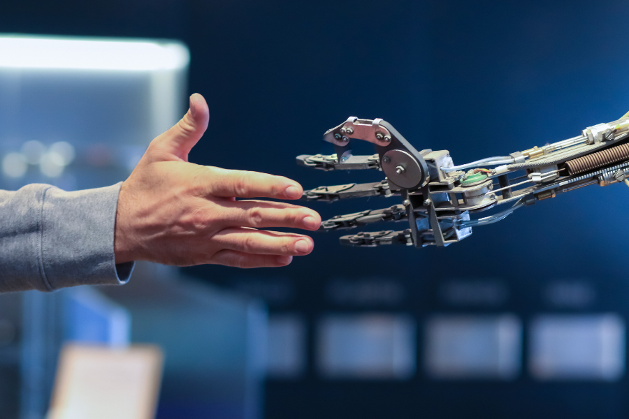 Close-up of a human hand reaching toward a robotic hand, symbolizing the trust, transparency, ethics, and explainability behind ScribePT’s assistive healthcare AI technology.
