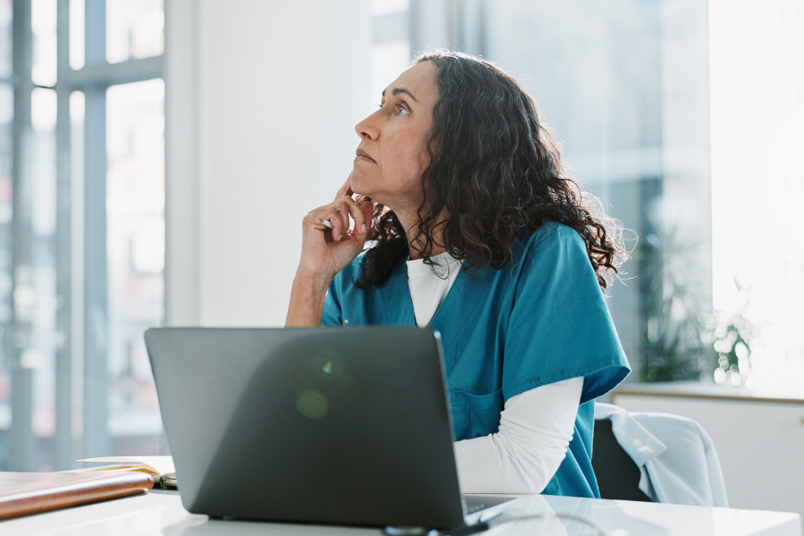 A physical therapy clinician sitting at a desk and thinking deeply while using a laptop to review unstructured clinical charting metrics, highlighting the need for ScribePT's specialized AI scribe platform to automatically capture complex rehab documentation and timed-code metrics.