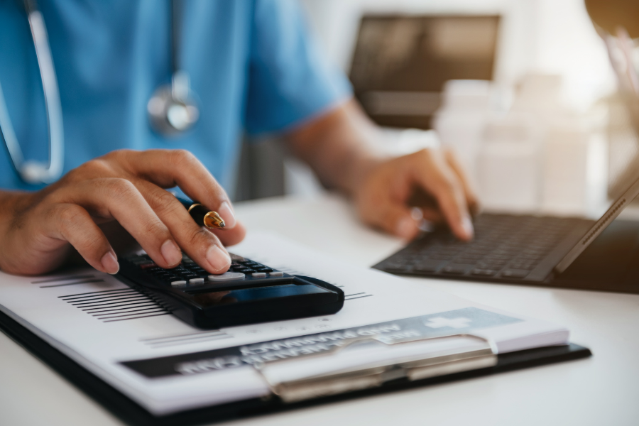 A healthcare executive in blue scrubs using a calculator and keyboard to analyze the total cost of ownership (TCO) of ambient AI scribes, demonstrating the contrast between heavy internal engineering overhead and scalable integration infrastructure like ScribePT.