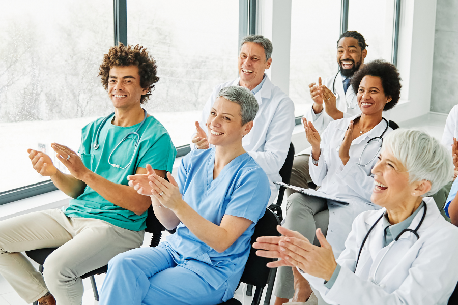 Smiling medical professionals applauding at a conference, representing the positive clinician response to ambient AI scribe technology and reduced EMR burnout.