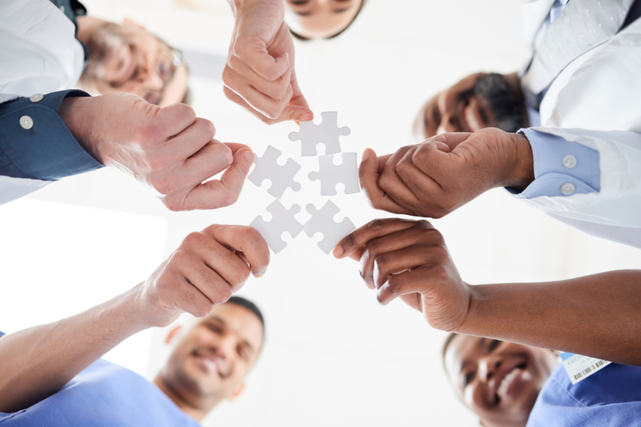 A team of medical professionals and physical therapists collaborating and assembling puzzle pieces, representing the seamless integration of AI documentation tools into clinical EMR workflows.